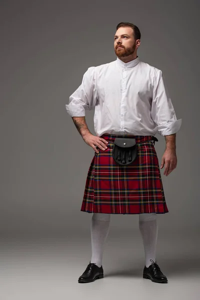 Шотландский Рыжий Мужчина Красном Килте Рукой Бедре Смотрит Сторону Сером — стоковое фото
