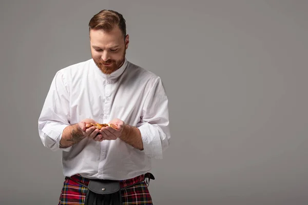 Scottish redhead man in red kilt with gold coins on grey background