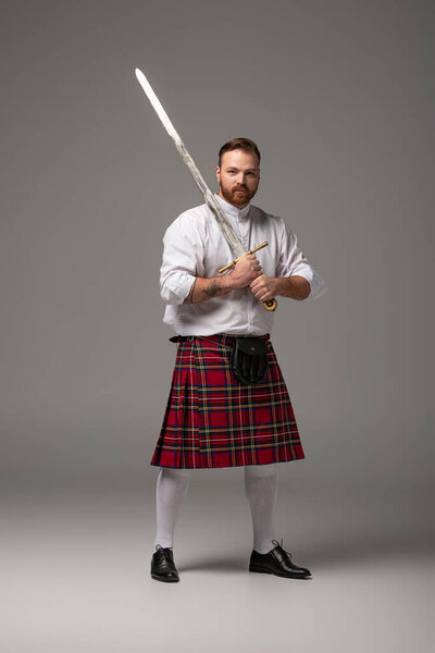 Scottish redhead man in red kilt with sword on grey background