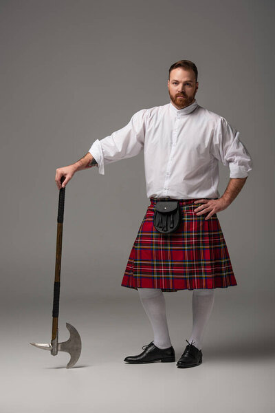Scottish redhead man in red kilt with battle axe on grey background