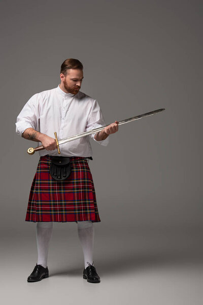 Scottish redhead man in red kilt with sword on grey background