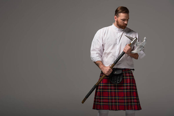 Scottish redhead man in red kilt with battle axe on grey background
