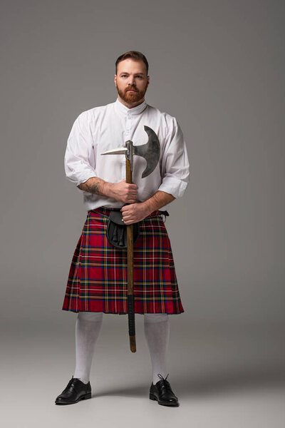 Scottish redhead man in red kilt with battle axe on grey background