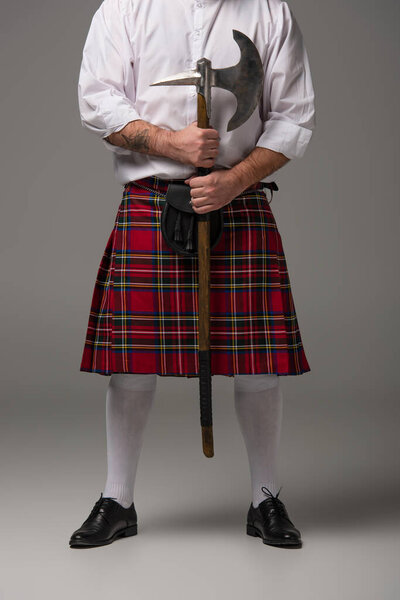 обрезанный вид шотландца в красном килте с боевым топором на сером фоне
