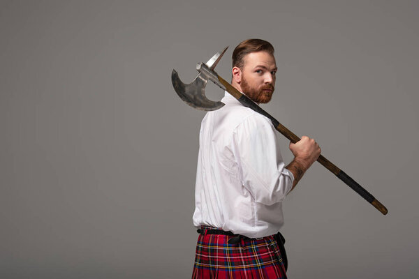 Scottish redhead man in red kilt with battle axe on grey background