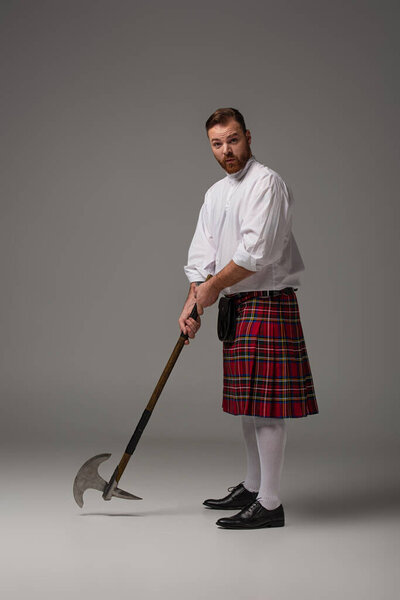 Scottish redhead man in red kilt with battle axe on grey background