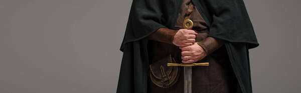 обрезанный вид средневекового шотландского рыцаря на камине с мечом в руках на сером фоне, панорамный снимок
