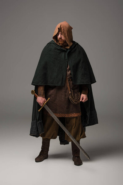Средневековый шотландский рыжий рыцарь в камине с мечом на сером фоне
