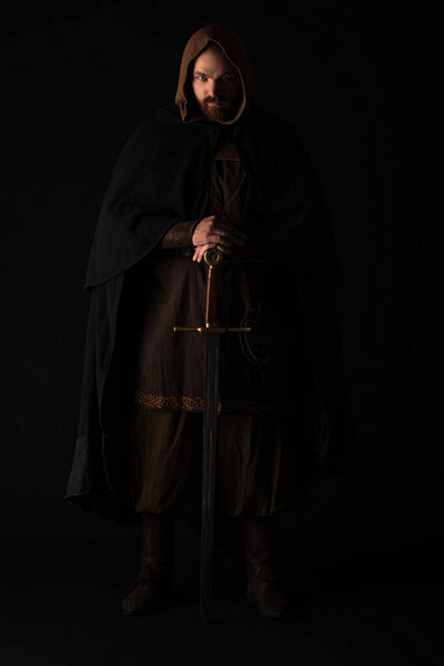 medieval Scottish man in mantel with sword in dark isolated on black