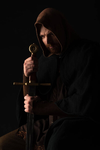 tense medieval Scottish man in mantel with sword in dark isolated on black