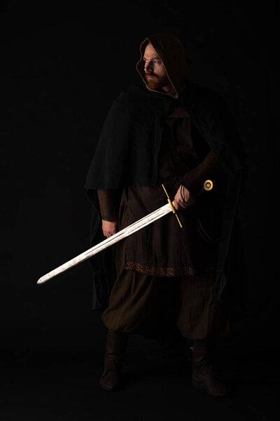 medieval Scottish man in mantel with sword in dark isolated on black