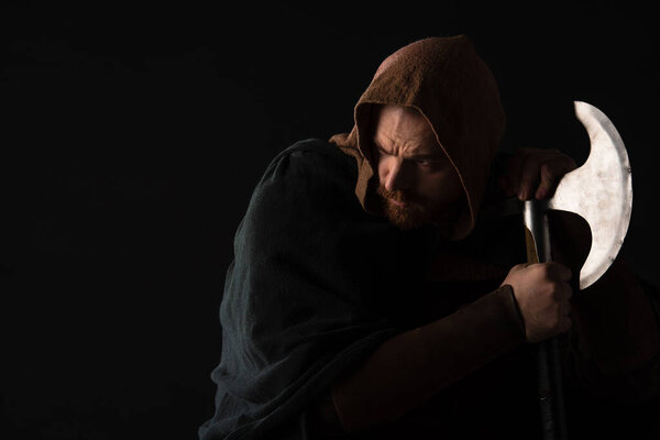 frowning medieval Scottish warrior with battle axe in mantel isolated on black