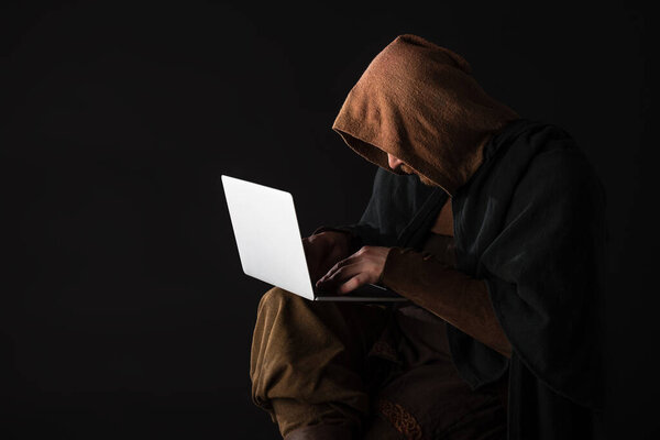 medieval Scottish man in mantel using laptop in dark isolated on black