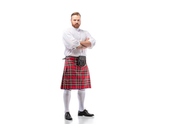 serious Scottish redhead bearded man in red tartan kilt with crossed arms on white background