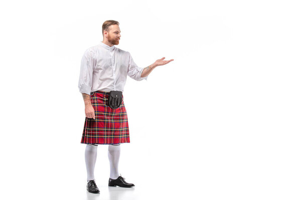 Scottish redhead bearded man in red tartan kilt pointing with hand on white background