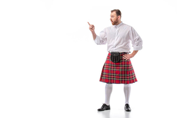 Шотландский рыжеволосый бородатый мужчина в красном тартановом килте указывает пальцем на белом фоне

