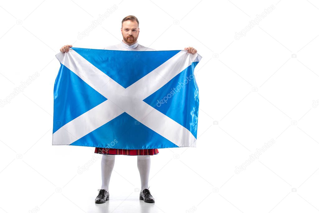 Scottish redhead man in red kilt with flag of Scotland on white background