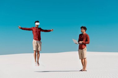 VR kulaklığa atlayan ve kumsalda dizüstü bilgisayarlı genç adam kolajı.
