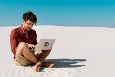young freelancer on sandy beach using laptop with stop virus sign against clear blue sky clipart