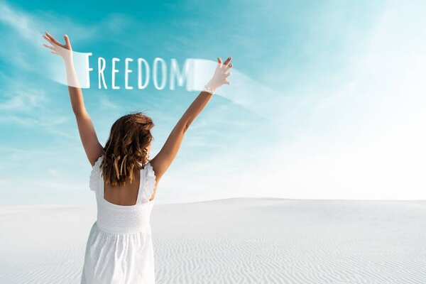 Вид сзади красивой девушки в белом платье с руками в воздухе на песчаном пляже с голубым небом, иллюстрация свободы
