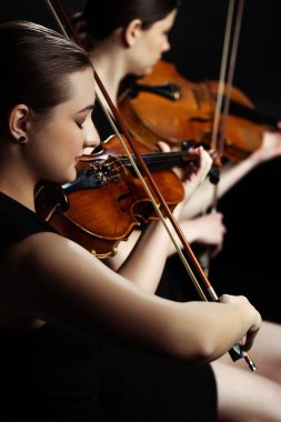 professional female musicians playing classical music on violins on dark stage, selective focus clipart