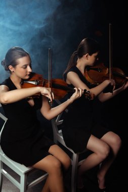 attractive professional musicians playing on violins on dark stage with smoke clipart