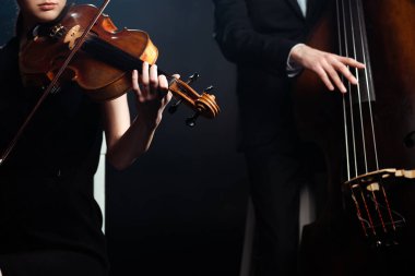 cropped view of professional musicians playing on violin and contrabass on dark stage clipart