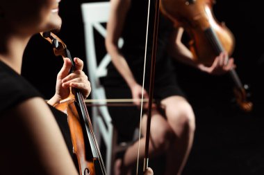 Koyu sahnede keman çalan kadın müzisyenlerin kısmi görüşü, seçici odaklanma