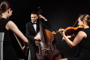 trio of happy musicians playing on double bass and violins isolated on black clipart
