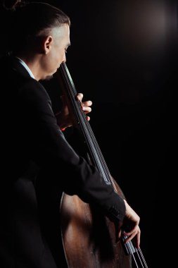 professional young musician playing on contrabass on dark stage clipart