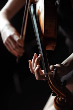 cropped view of female musician playing on violin on dark stage clipart