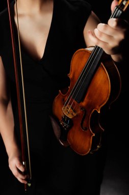 cropped view of female musician holding violin on dark stage clipart