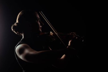 silhouette of female musician playing on violin on dark stage clipart