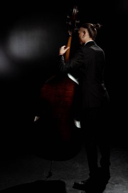 back view of professional musician playing on contrabass on dark stage clipart