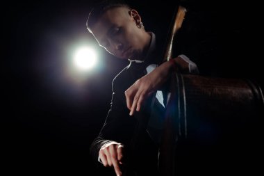 professional musician playing on double bass on dark stage with back light clipart