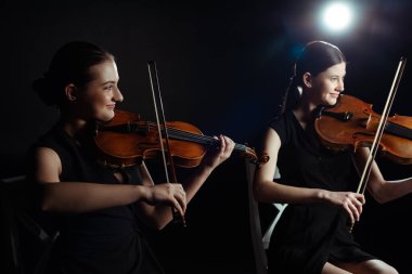 happy attractive musicians playing on violins on dark stage with back light clipart