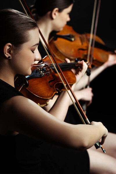 профессиональные женщины-музыканты, играющие классическую музыку на скрипках на темной сцене, избирательный фокус

