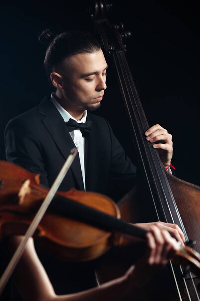 two professional musicians playing on violin and contrabass on dark stage 