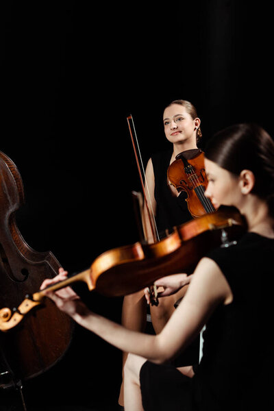 professional positive musicians playing classical music on violins on dark stage 