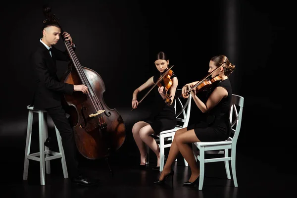 三位专业音乐家在小提琴上演奏古典音乐 在黑暗舞台上演奏对比度低音 — 图库照片