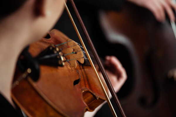 cropped view of professional musicians playing on musical instruments on dark stage, selective focus