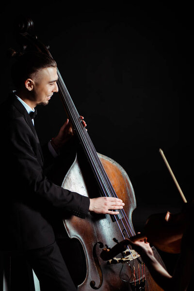 happy professional musicians playing on violin and contrabass on dark stage 