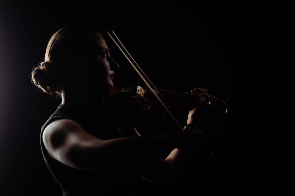 silhouette of female musician playing on violin on dark stage