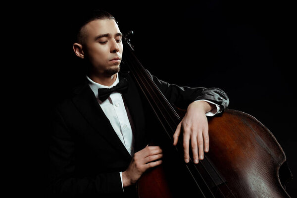 young musician playing on double bass isolated on black