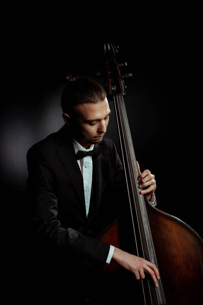 professional musician playing on double bass on dark stage