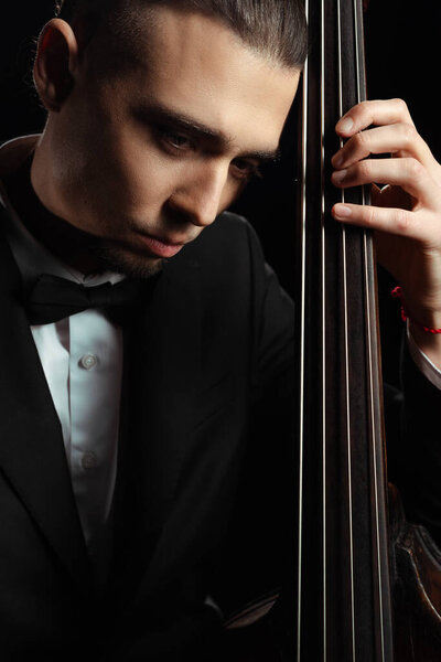 professional handsome musician playing on contrabass isolated on black