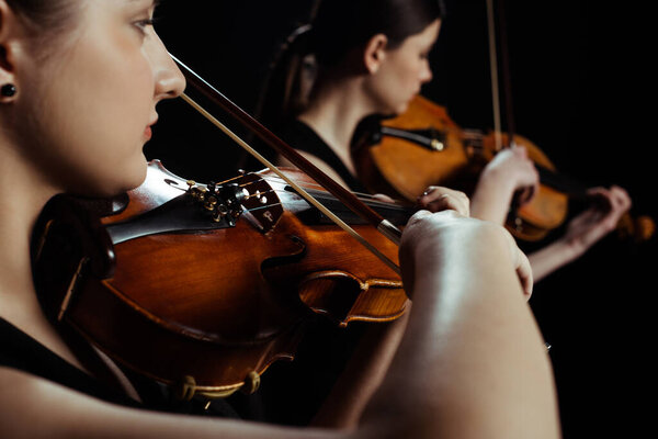 young professional musicians playing classical music on violins on dark stage 