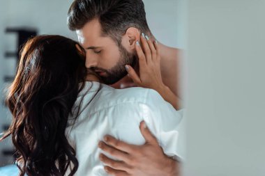 selective focus of sexy young brunette woman in shirt hugging man with bare torso and closed eyes clipart