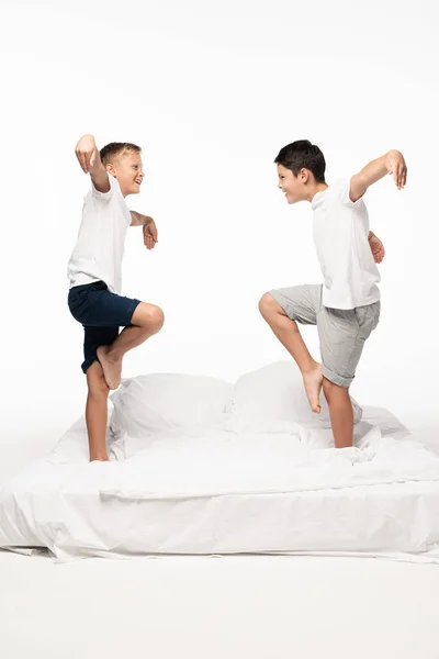 Zwei fröhliche Brüder, die Vögel imitieren, während sie auf weißem Hintergrund auf dem Bett stehen — Stockfoto