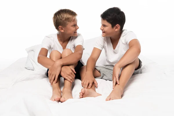 Deux frères joyeux assis sur le lit et se regardant isolés sur blanc — Photo de stock